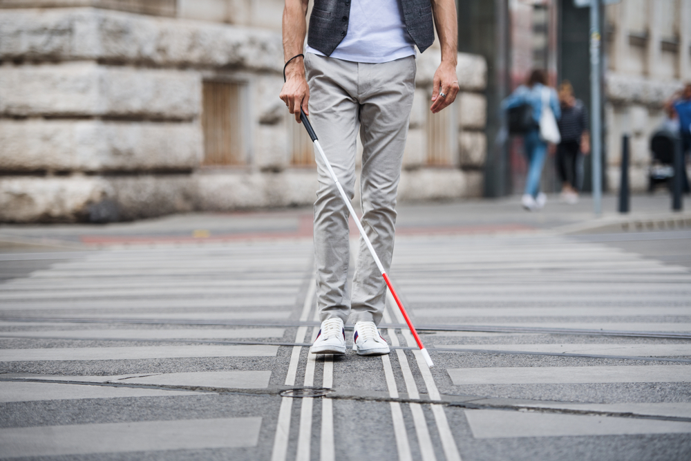 Homem com deficiência visual atravessando a rua com bengala.